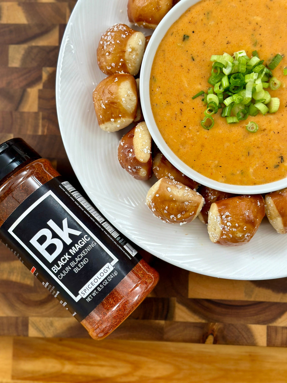 Bowl of Black Magic Beer Cheese surrounded by pretzel bites and a jar of Spiceology Black Magic