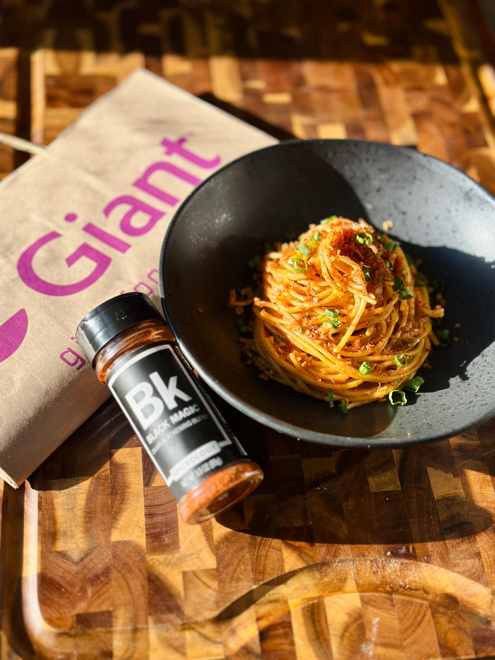 Bowl of Black Magic Garlic Crab Pasta next to a Giant grocery bag and bottle of Spiceology Black Magic