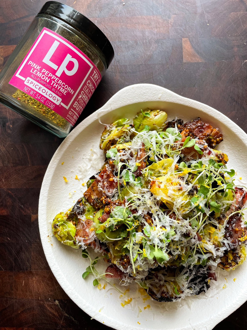 Plate of roasted Brussels sprouts with a jar of Spiceology's Pink Peppercorn Lemon Thyme