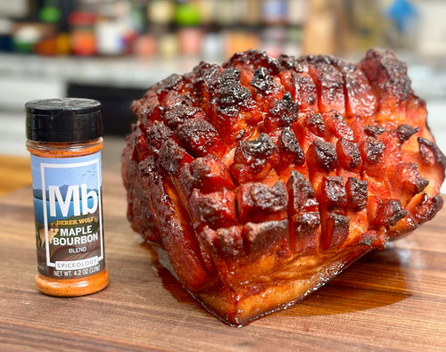 Finished roasted ham on cutting board next to a bottle of Spiceology Maple Bourbon.