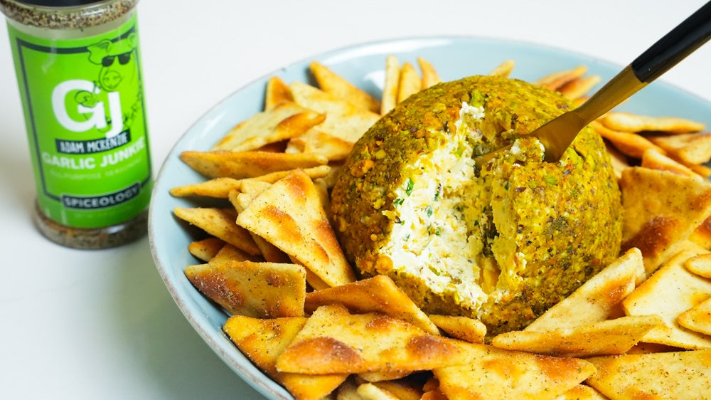 Plate with Garlic Junkie Pistachio Cheeseball surrounded by pita chips next to a jar of Spiceology Garlic Junkie