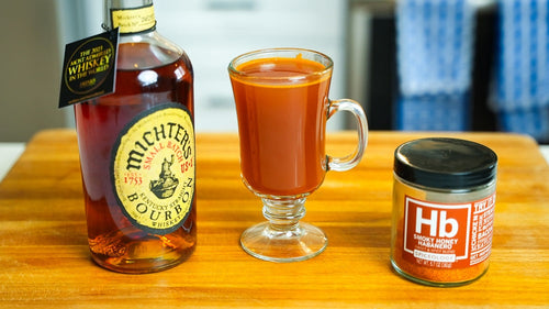 Cider Hot Toddy in a glass mug next to Spiceology Smoky Honey Habanero jar and Michter's bourbon bottle