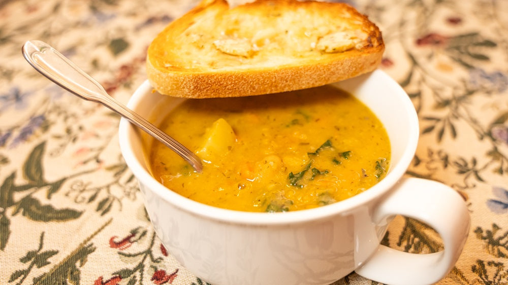 Cup of Rosemary Dijon Garlic, White Bean and Potato Soup with spoon in soup and topped with toasted bread