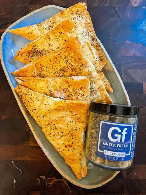 Plated Greek Freak Spinach, Feta and Ricotta-Stuffed Phyllo Pockets next to a jar of Spiceology Greek Freak Mediterranean blend