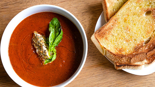 Tomatador and Smokey Honey Habanero charred tomato soup in a bowl next to toasted bread.