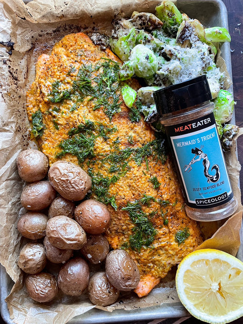 Roasted Mustard Trout and potatoes on a sheet pan next to a Spiceology X MeatEater Mermaid's Trident jar