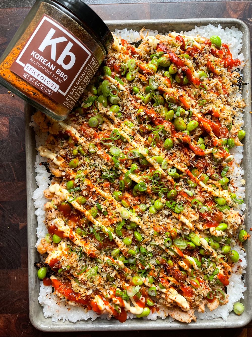 Sheet pan sushi bake with layers of ingredients like shrimp, edamame, and more next to a Spiceology Korean BBQ jar.