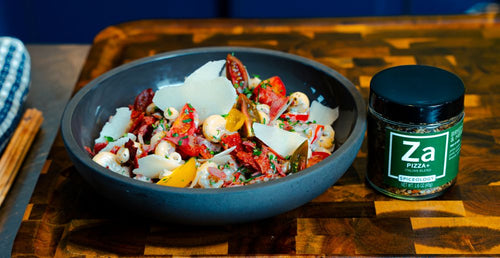 Bowl of Pepperoni Pasta Salad on a wooden cutting board next to a jar of Spiceology Pizza+ seasoning