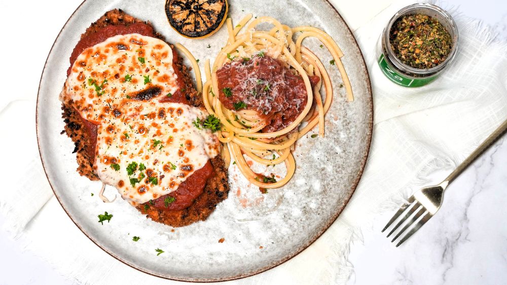 Plated Chicken Parmesan with spaghetti next to an open jar of Spiceology Pizza+ seasoning
