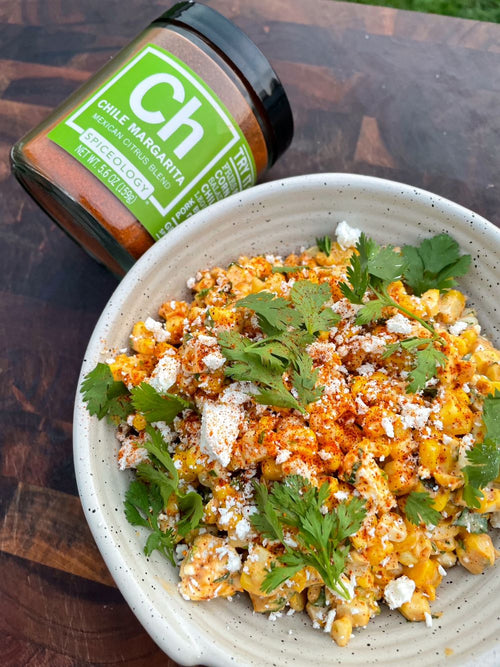 Bowl of Elote-Inspired Corn topped with cotija and cilantro Salad next to a jar of Spiceology Chile Margarita blend