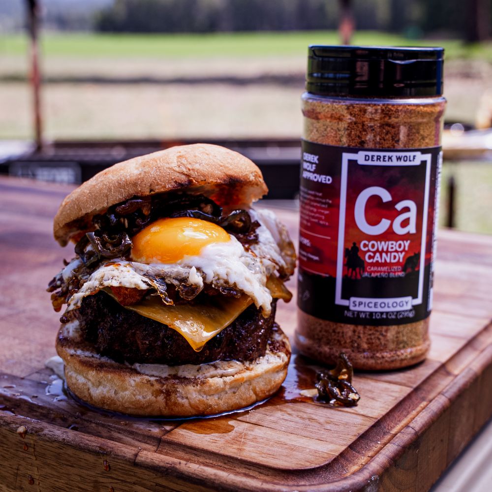 Stacked breakfast burger with bacon and a sunnyside egg next to a jar of Spiceology Cowboy Candy seasoning
