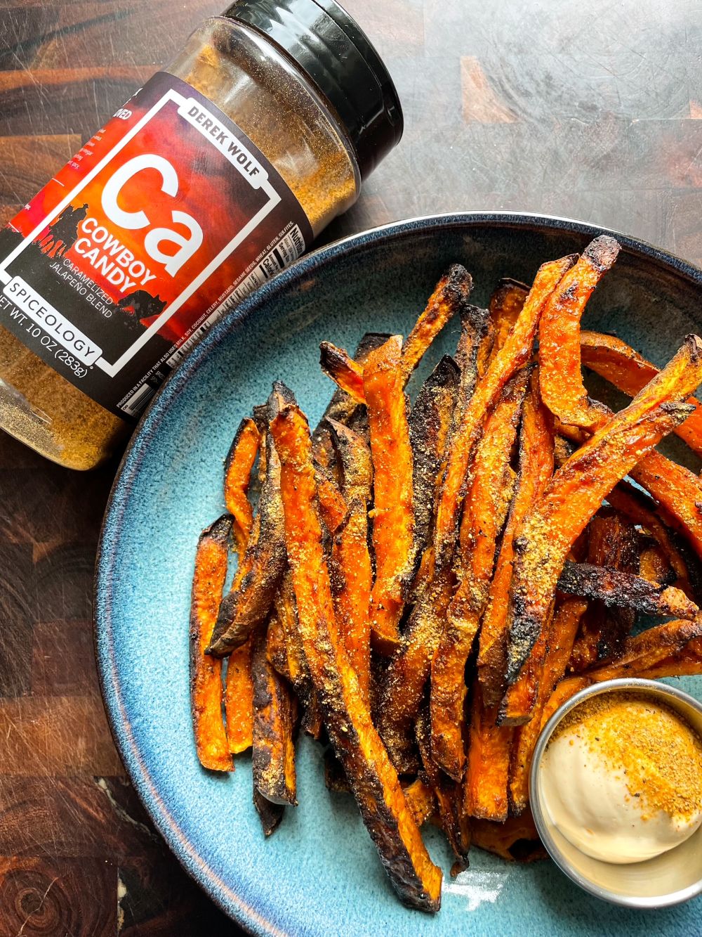 Plated oven-baked sweet potato fries next to a jar of Spiceology Cowboy Candy blend