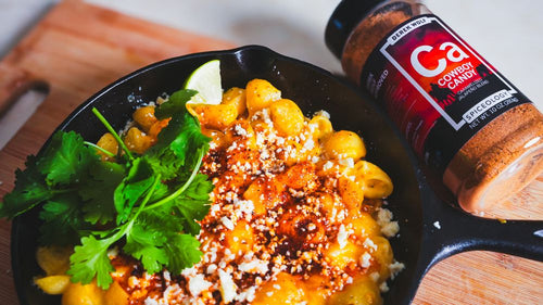 Cast iron of Elote-Inspired Mac and Cheese next to a jar of Spiceology Cowboy Candy blend