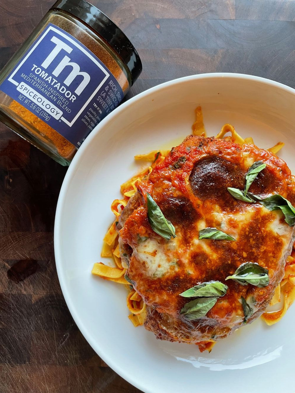 Plated Chicken Parmesan next to a jar of Spiceology Tomatador blend