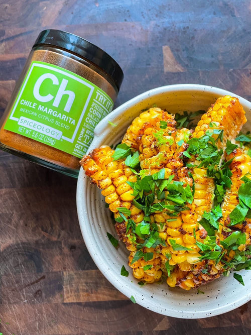 Bowl of corn ribs topped with cilantro next to a jar of Spiceology Chile Margarita blend