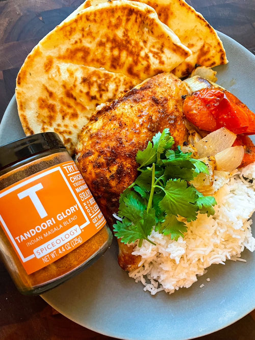 Plated roasted half chicken with rice, tomatoes and cilantro next to a jar of Spiceology Tandoori Glory