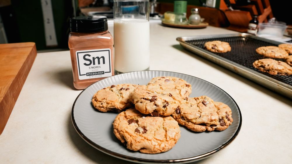 Plate of S'mores Brown Butter Chocolate Chip Cookies on plate next to a glass of milk and jar of Spiceology S'mores blend