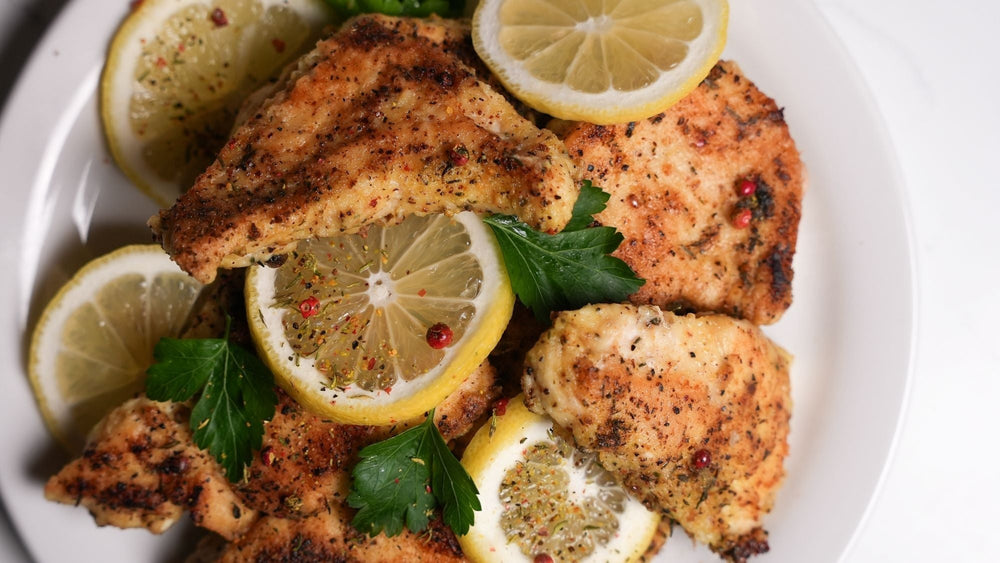 Pink peppercorn lemon thyme chicken served with sliced lemons and fresh herbs on a white plate