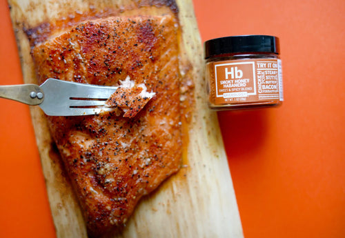 smoky honey habanero cedar plank salmon served on plank with fork bite and jar of spices