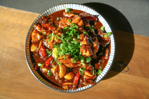 Bowl of Sticky Bourbon Brown Ale Three Cup Chicken featuring braised chicken, garlic, dried chiles, and green onions coated in a sweet and savory bourbon brown ale glaze.