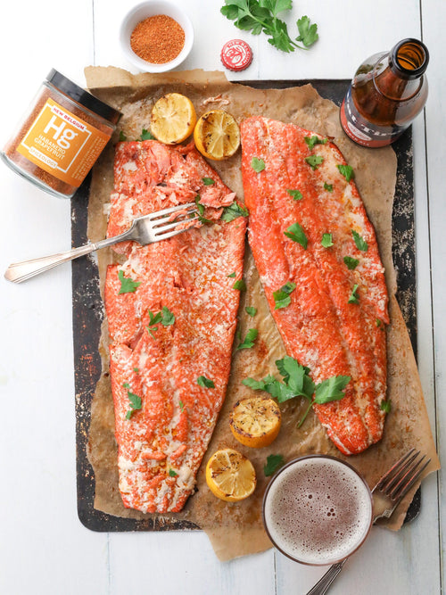 2 salmon fillets on parchment with a jar of spice, bottle of beer and glass of beer