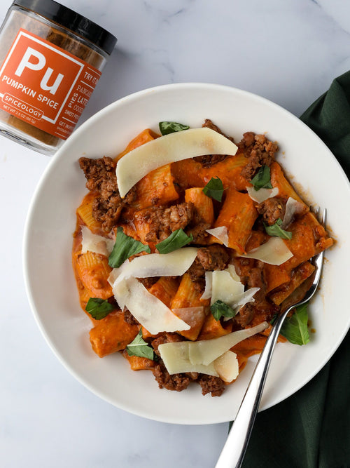 a white plate with pumpkin alla vodka pasta, sausage and a jar of spiceology pumpkin spice blend