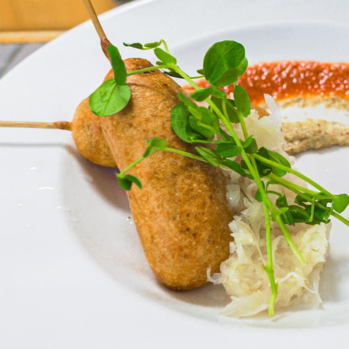 Bratwurst corn dogs on plate with tomato jam, sauerkraut and sprouts