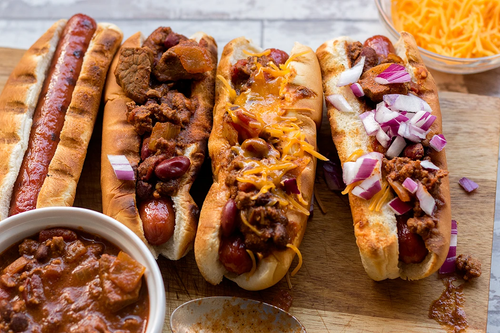 Cowboy chili dogs lined up topped with onion and cheddar cheese