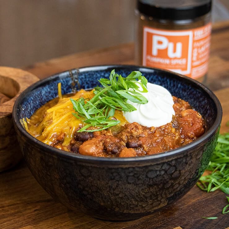 pumpkin spice turkey chili in bowl topped with sour cream, green onion, cheese