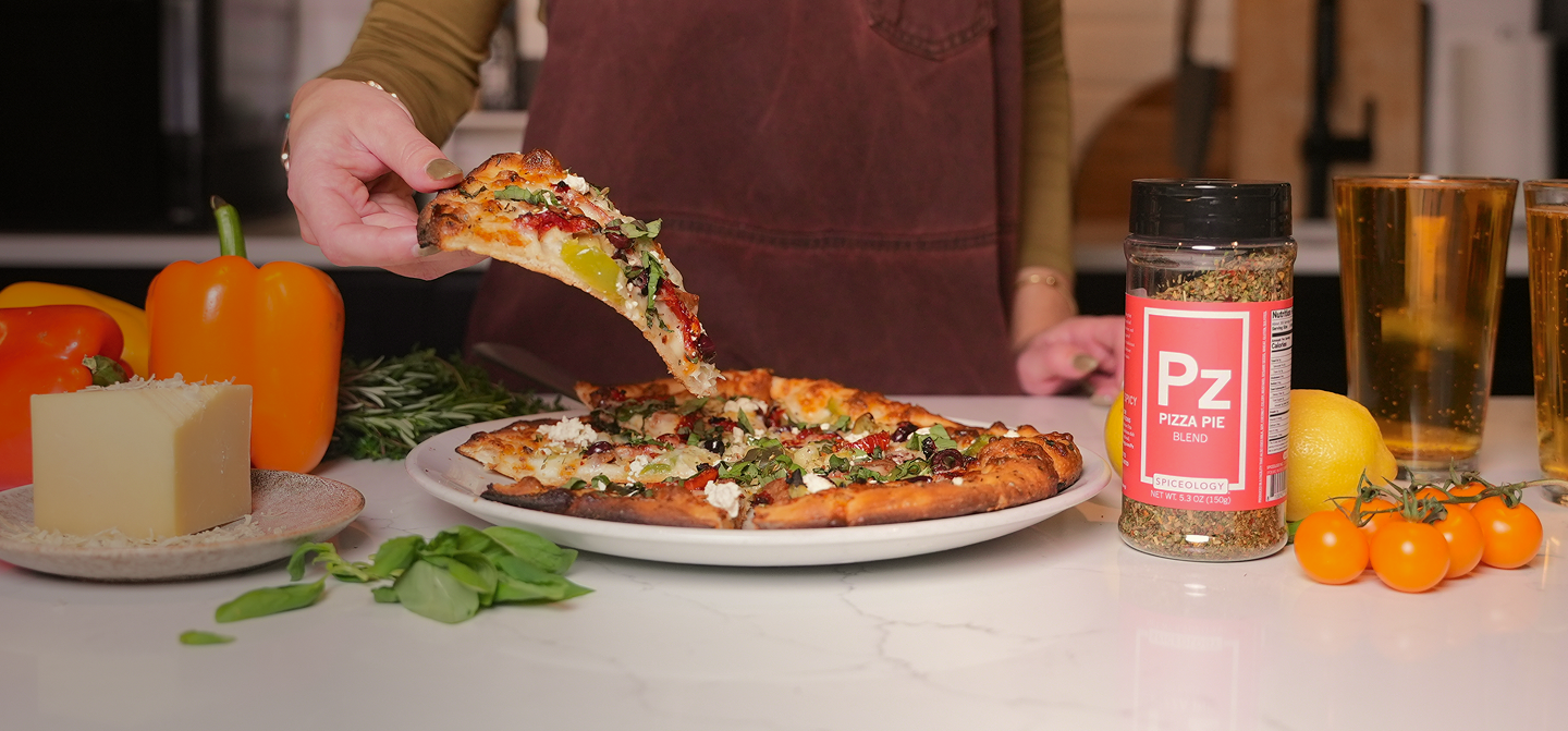 Person serving pizza with a bottle of Pizza Pie seasoning on a table.