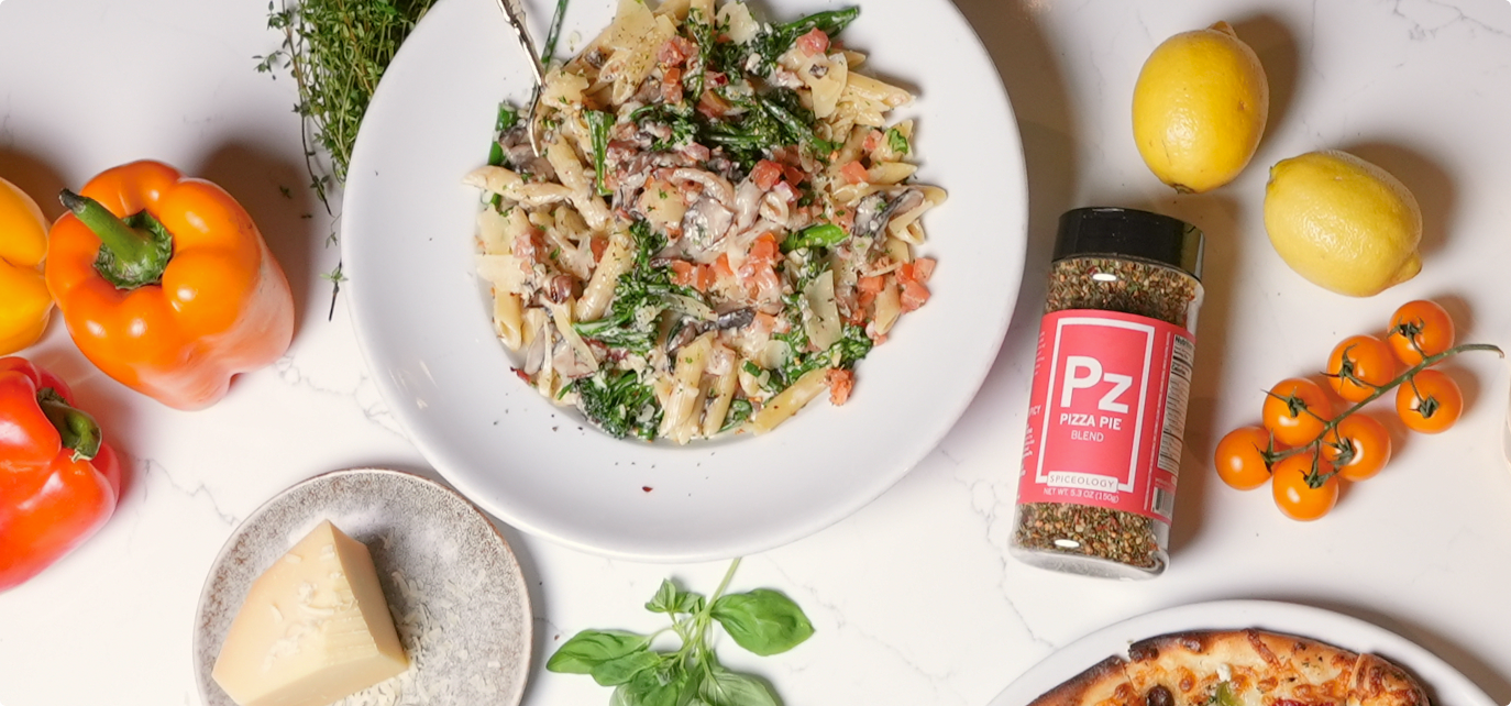 Pasta dish with vegetables and a container of Spiceology Pizza Pie seasoning on a white surface.