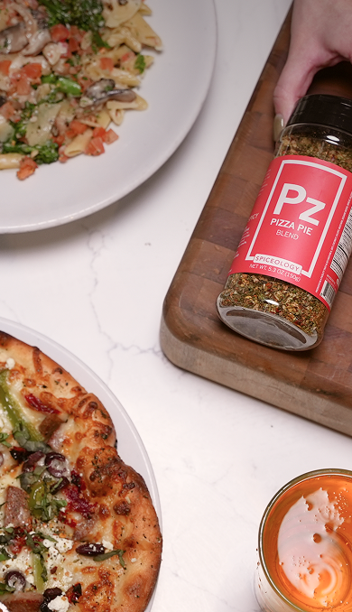 Pizza with a bottle of Spiceology Pizza Pie seasoning on a wooden board, with a plate of pizza and a small container in the background.