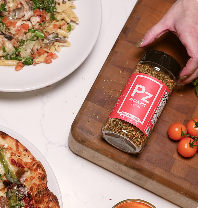 Bottle of Spiceology Pizza Pie seasoning on a wooden cutting board with food in the background