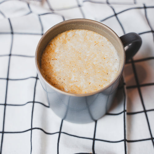 Hot coffee latte in a white ceramic mug on a white cloth napkin viewed from above