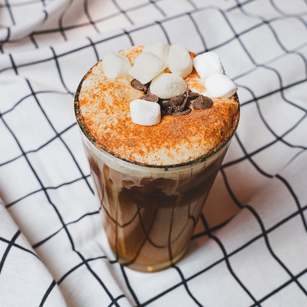 Iced coffee with whipped cream topping in a glass mug on a plaid cloth napkin