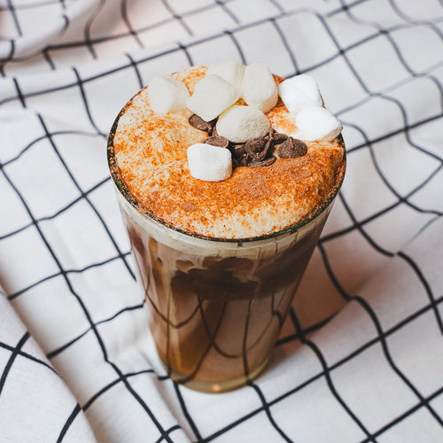Iced coffee with whipped cream topping in a glass mug on a plaid cloth napkin