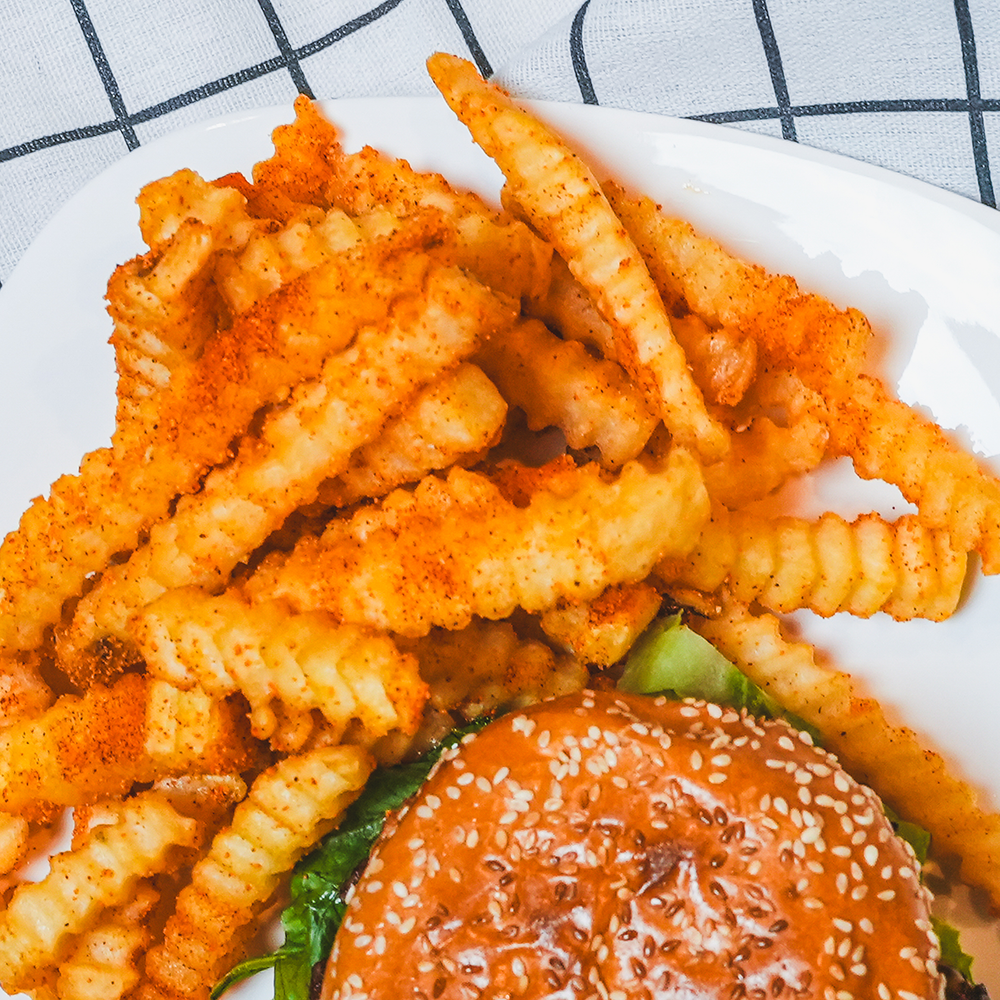 Overhead view of crispy crinkle-cut fries beside a burger on a plaid cloth surface