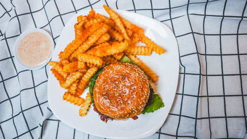 Overhead view of a burger and crispy crinkle fries with a dipping sauce on a white plate