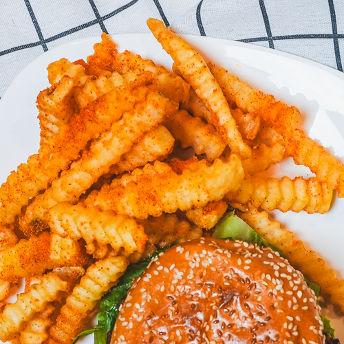 Overhead view of crispy crinkle-cut fries beside a burger on a plaid cloth surface