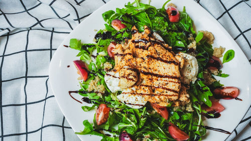 Overhead view of a salad with grilled protein slices on a white ceramic plate