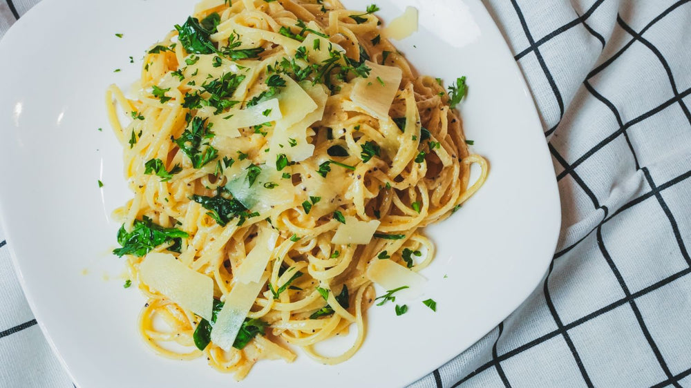 Overhead view of a pasta dish tossed with garlic herb sauce and parsley on a white plate