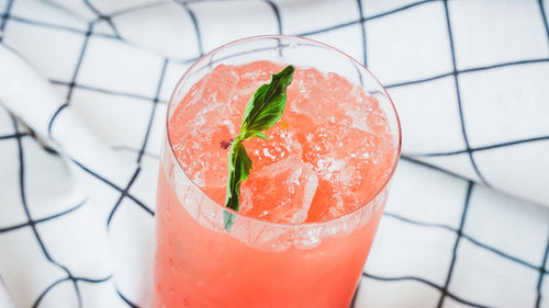 Overhead view of a pink watermelon cocktail with a mint leaf garnish in a glass