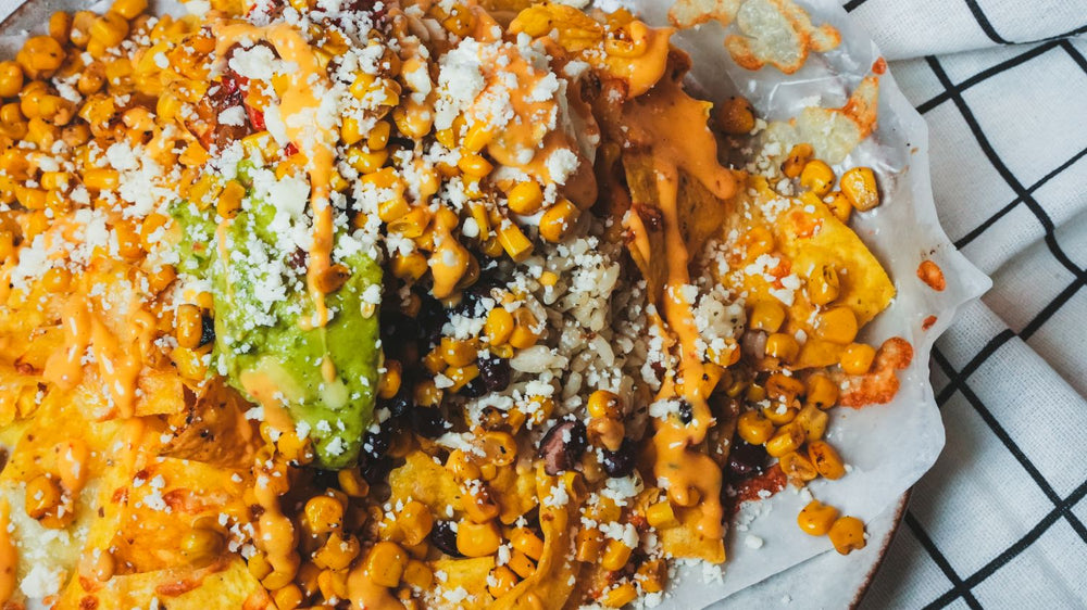 Overhead view of loaded nachos with avocado, cheese, and garnishes on a plaid cloth background