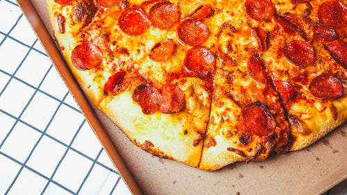 Overhead view of a loaded pepperoni pizza with crispy edges on a pizza stone