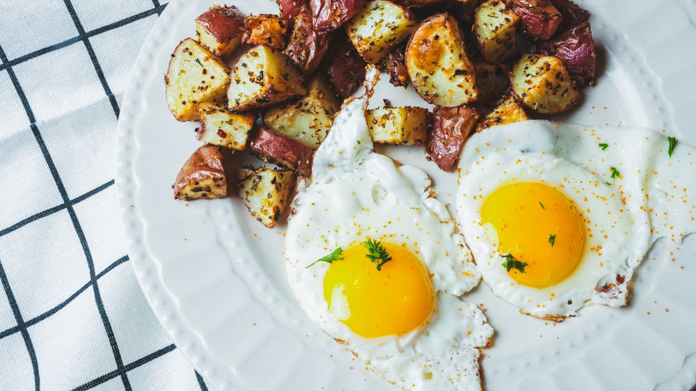 Overhead view of two sunny-side-up eggs with roasted potatoes and vegetables on a plaid cloth