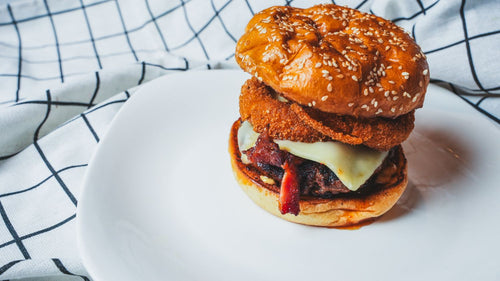 Close-up side view of a burger with melted cheese and onion rings on a sesame seed bun