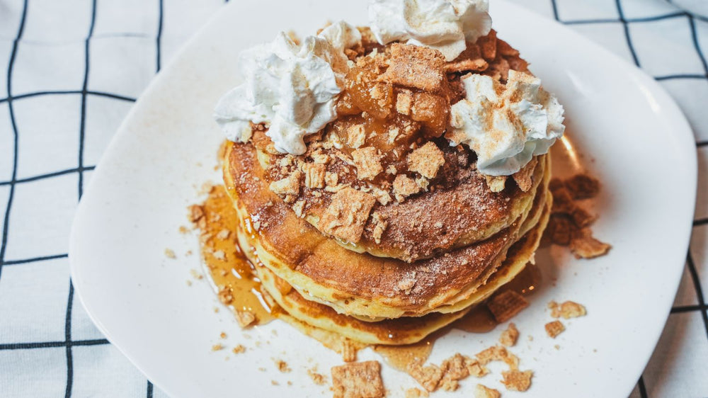 Stack of fluffy pancakes topped with whipped cream and crumbled brown-sugar topping on a white plate