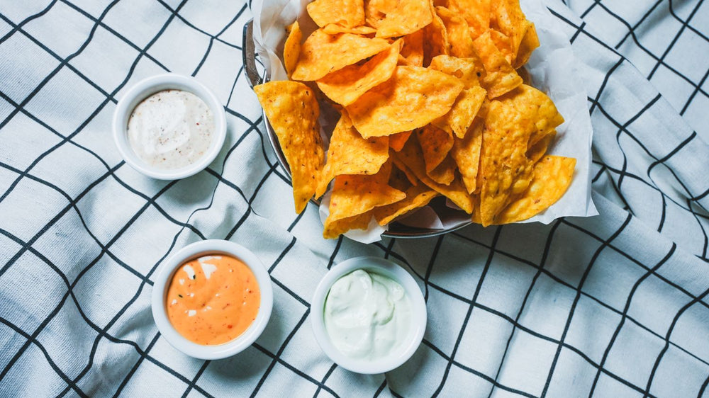 Overhead view of tortilla chips with two dipping sauces in small bowls on a light blue surface
