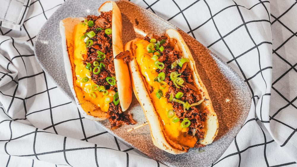 Chili-topped hot dog or loaded sausage with green garnish on parchment paper