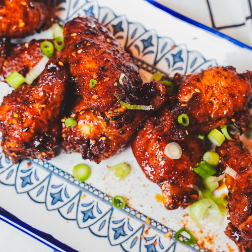 Overhead view of glazed chicken wings on a blue and white patterned plate with a plaid cloth
